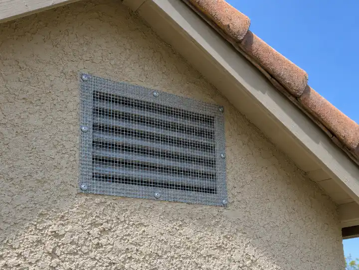 Gable vent on a stucco house covered with galvanized hardware cloth fastened at the edges